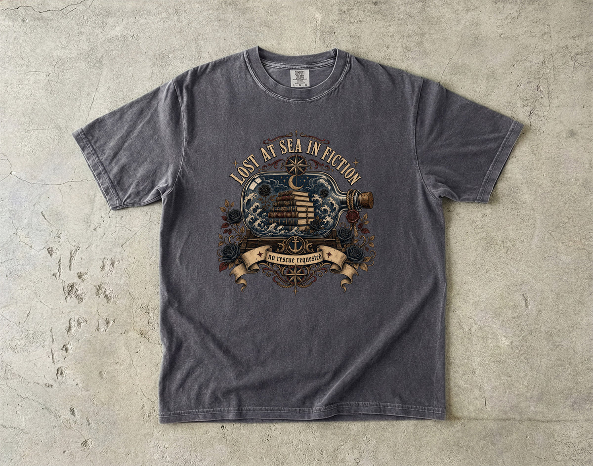 A dark gray crewneck t-shirt with a vintage nautical graphic reading 'Lost at Sea in Erection' and 'To Those Who Follow', laid flat on a textured concrete surface.