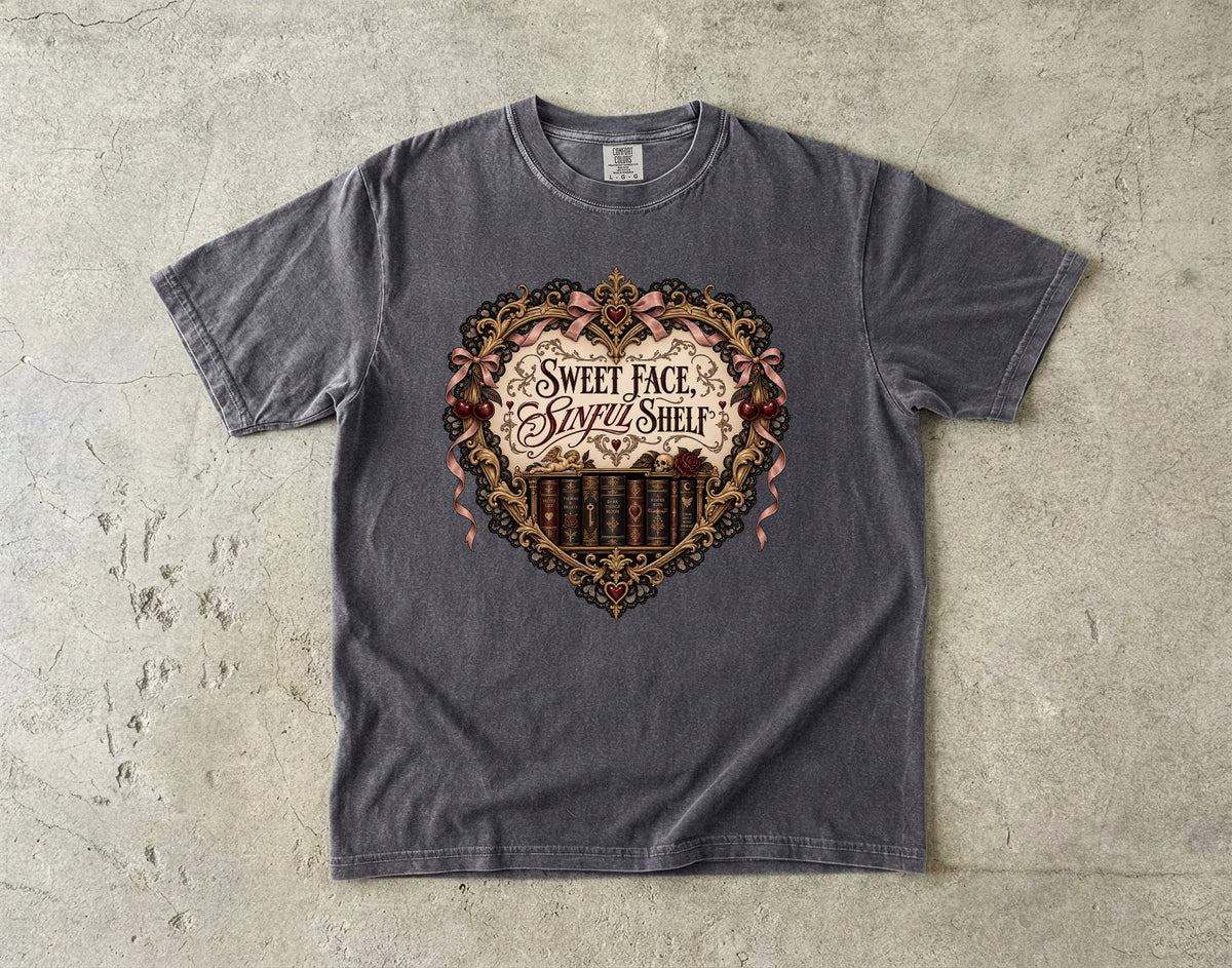 A dark gray heather t-shirt laid flat on a textured concrete surface, featuring a large heart-shaped graphic with the text 'SWEET FACE, SAVED SHELF' and a barbell design.