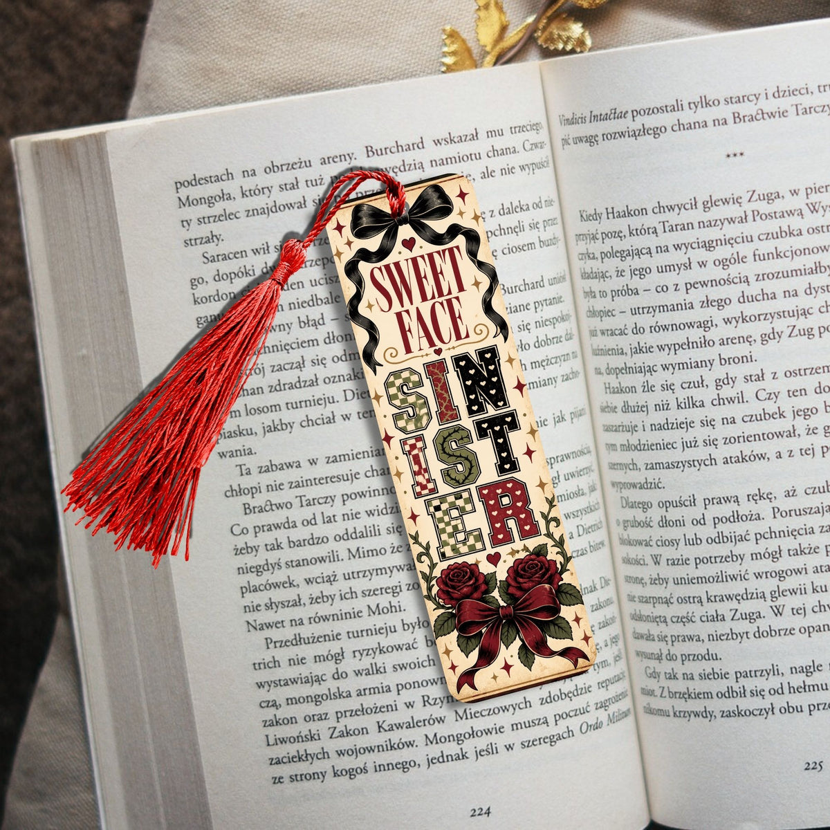 A decorative wooden book bookmark with a red tassel and red roses, reading 'READ MORE IN THE BIBLE' in Polish, placed on an open book.