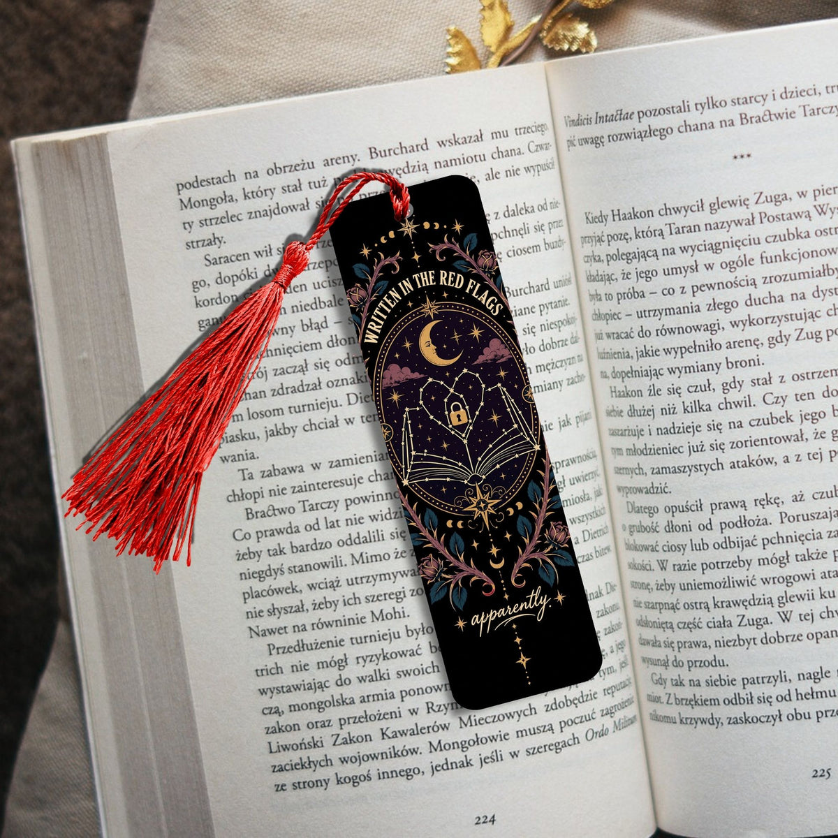 A black leather bookmark with gold lettering reading 'WITNESS IN THE RED HEART' and 'POLSKIE ZESPOLY WOJENNE', tied with a red tassel, resting on an open book with another book in the background.