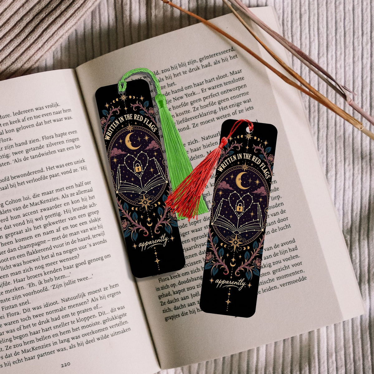 Two decorative bookmarks with a dark celestial design featuring a crescent moon and stars, styled on an open book with a green tassel bookmark and wooden chopsticks nearby.