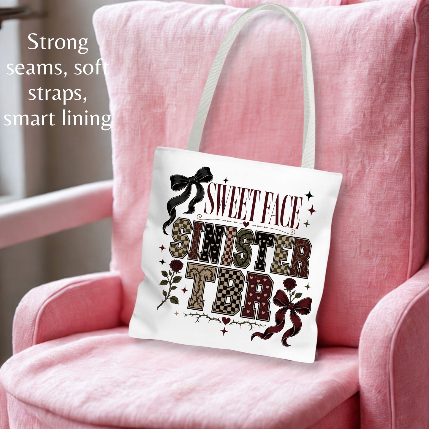 A white canvas tote bag with a 'Sweet Sister Face' graphic print, displayed on a pink armchair. The bag has white shoulder straps and features a graphic with the words 'SWEET FACE SINISTER TONIGHT' in patterned and black lettering, accented with bows and stars.
