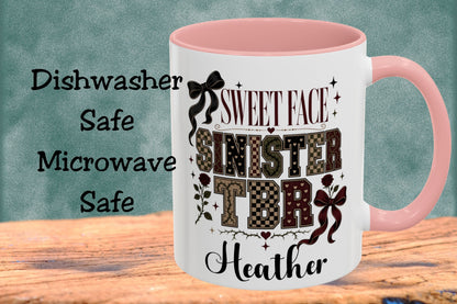 A white ceramic mug with a pink interior and handle, featuring a custom printed design that reads 'SWEET FACE SINISTER TITHE Heather' with decorative bows and patterned lettering. The mug is displayed on a wooden surface against a textured teal background, with text on the left stating 'Dishwasher Safe Microwave Safe'.