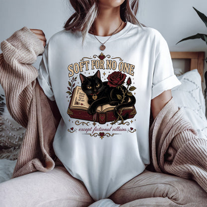 A woman wearing a white graphic t-shirt with a black cat and rose design, styled with a beige knit cardigan in a cozy bedroom setting.