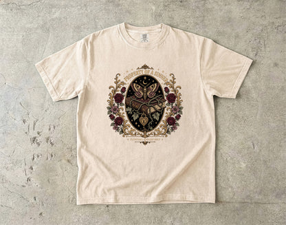 A cream-colored short-sleeve t-shirt with a detailed gothic-style graphic print featuring a clockwork owl, roses, and the text 'TIME IS A LOST CAUSE' on a textured gray concrete background.