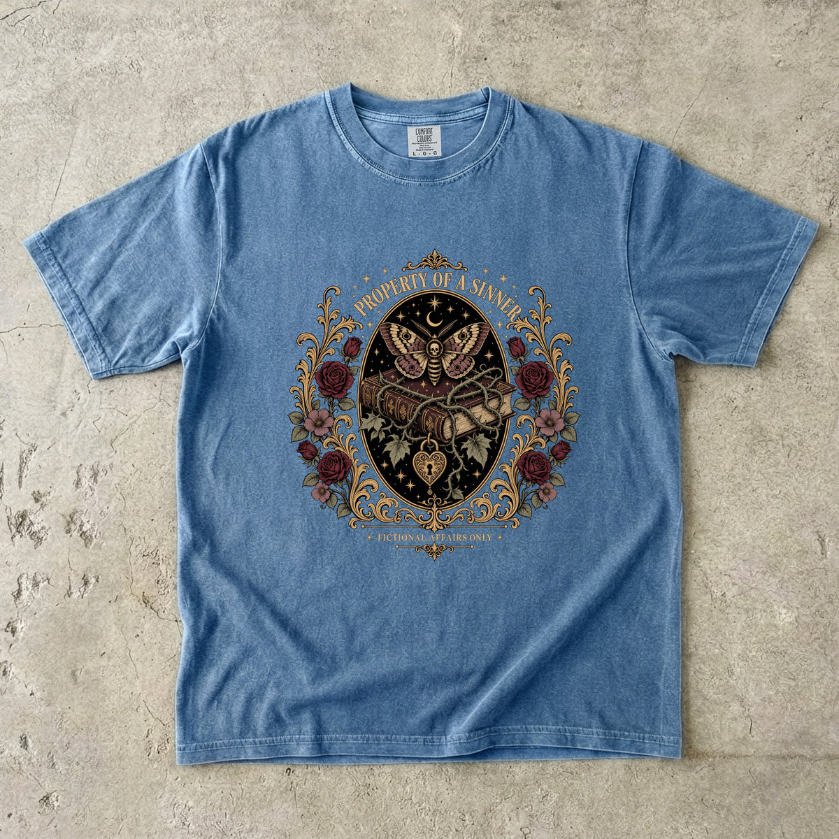 A light blue short-sleeve t-shirt with a detailed gothic graphic print featuring a skeleton, roses, and a crescent moon, laid flat on a textured concrete surface.