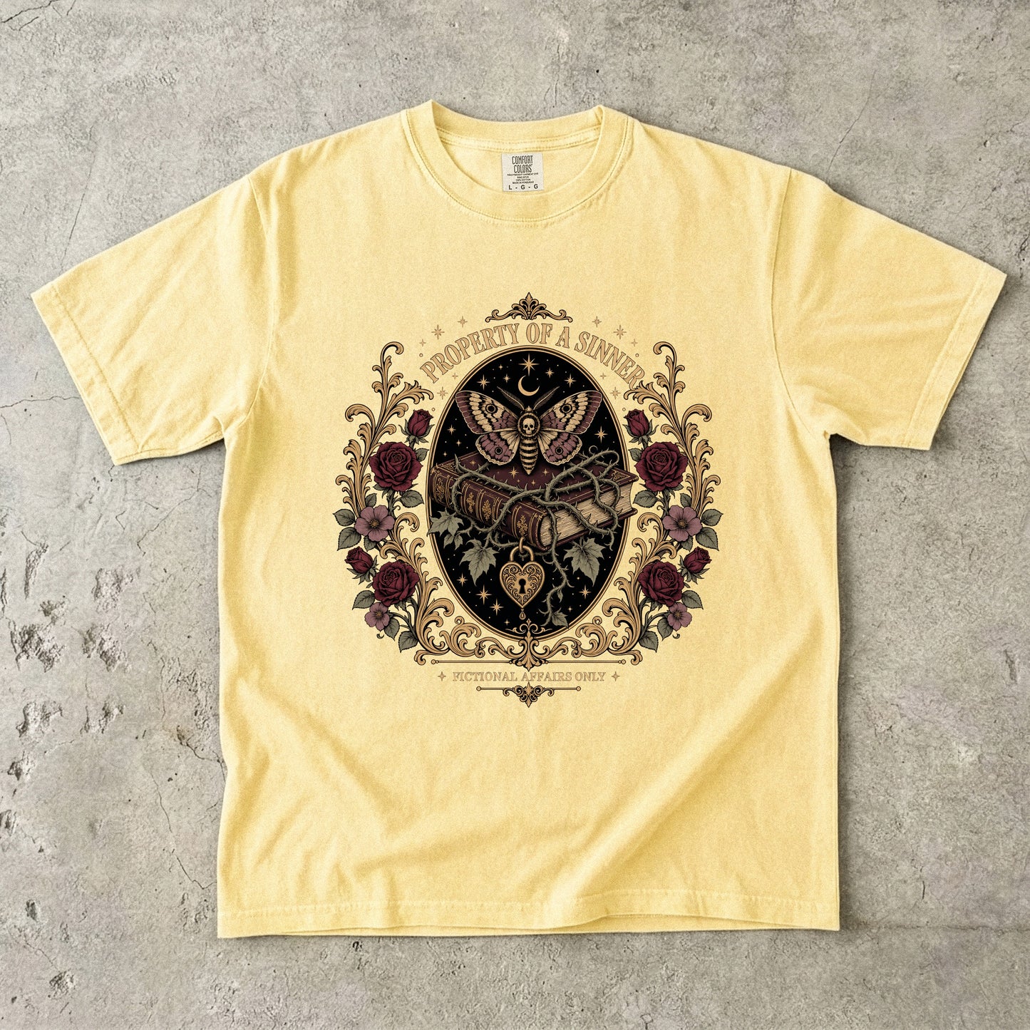A pale yellow short-sleeve t-shirt with a detailed gothic-style graphic print on the front, laid flat on a textured gray concrete surface.