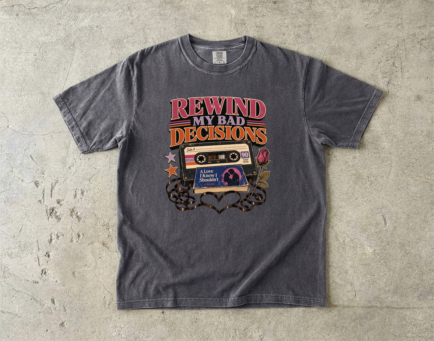 A dark gray graphic t-shirt laid flat on a textured concrete surface. The shirt features a retro cassette tape graphic with the text 'REWIND MY BAD DECISIONS' in red and orange, along with 'The Powerpuff Girls' logo and decorative elements.