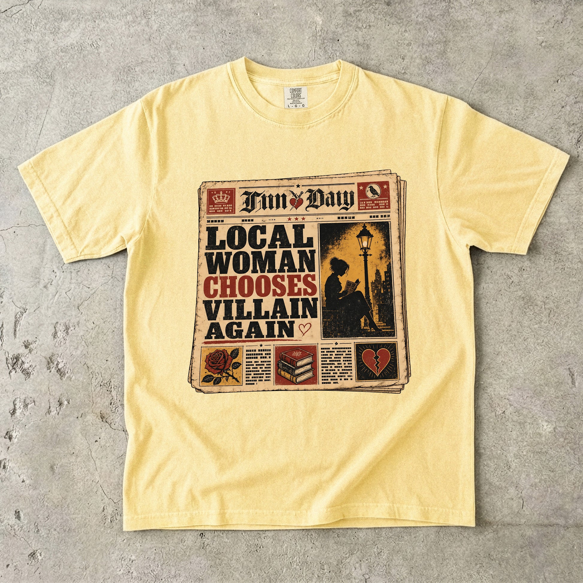 A pale yellow short-sleeve t-shirt laid flat on a textured gray concrete surface. The front of the shirt features a large graphic print styled like a newspaper front page with the text 'LOCAL WOMAN CHOOSES VILLAIN AGAIN' and the title 'Fun Day'.