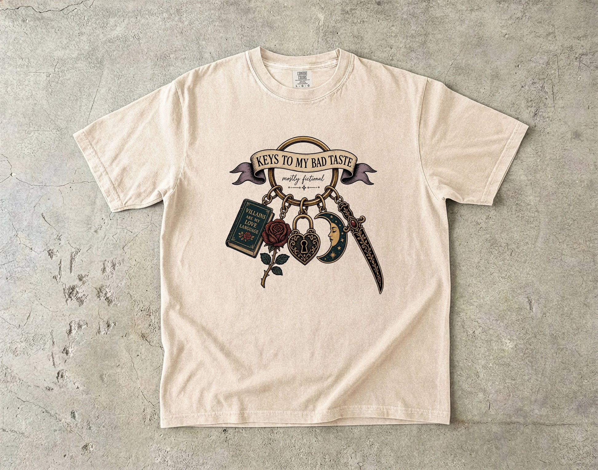 A cream-colored short-sleeve t-shirt with a graphic print of 'Keys to My Bad Taste' hanging keys, laid flat on a textured gray concrete surface.
