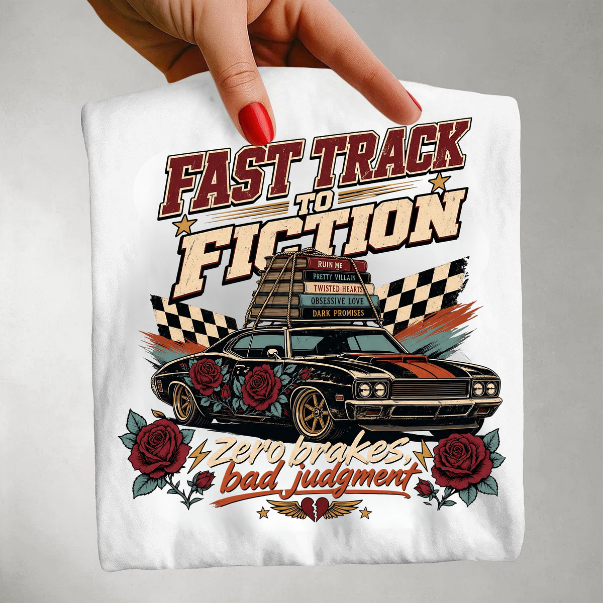 A hand with red nail polish holds up a white t-shirt featuring a retro-style graphic of a black muscle car with red roses, checkered flags, and the text 'FAST TRACK TO FICTION' and 'Zero makes bad judgment'.