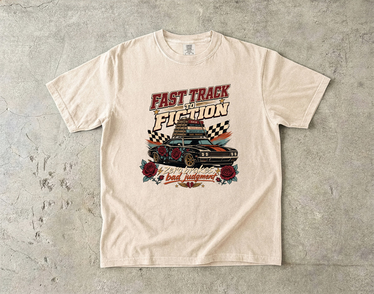 A cream-colored short-sleeve t-shirt with a vintage-style graphic print on the front, laid flat on a textured gray concrete surface. The graphic features the text 'FAST TRACK THE FICTION' above an illustration of a race car with checkered flags and roses.
