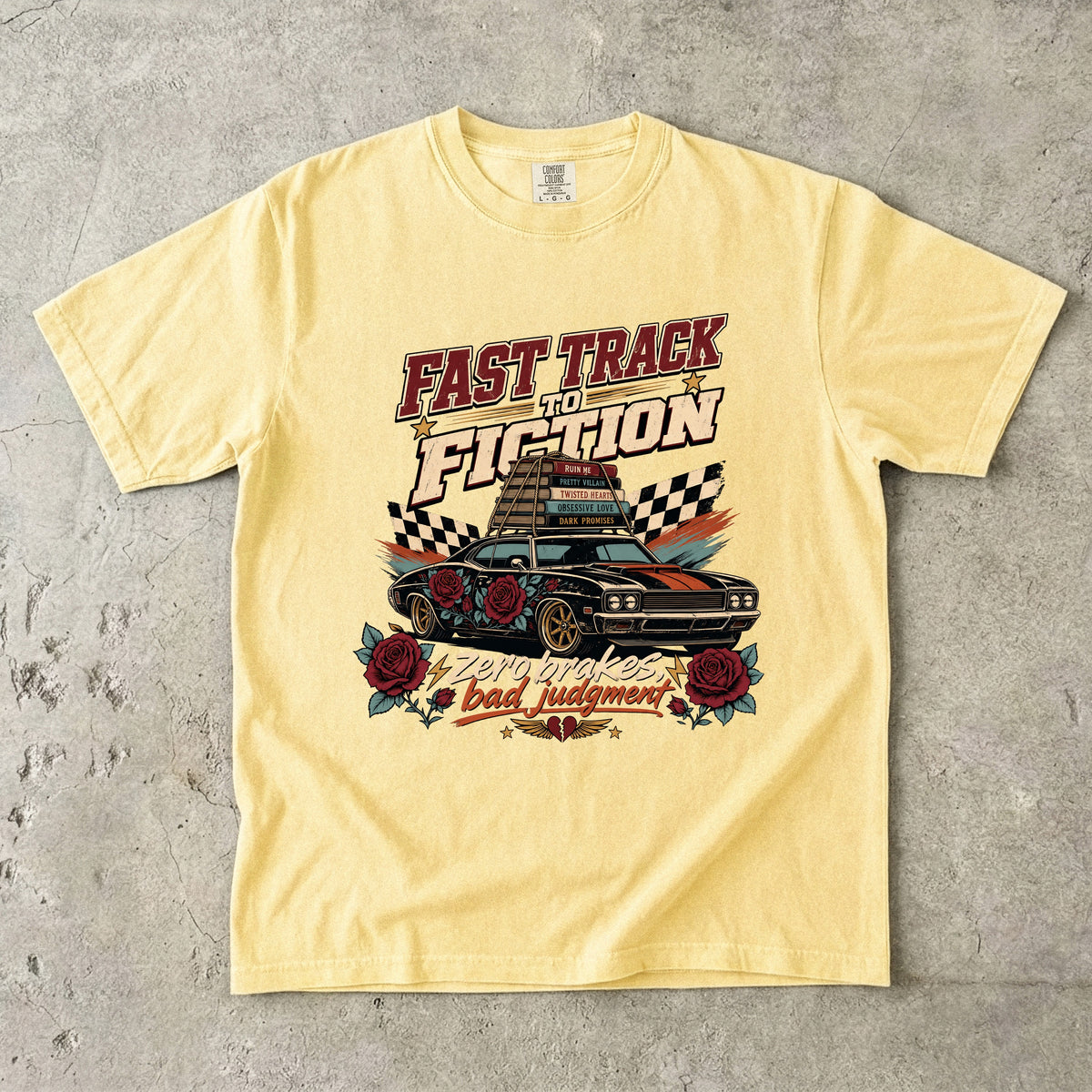 A pale yellow graphic t-shirt laid flat on a textured gray concrete surface. The shirt features a retro-style racing graphic with the text 'FAST TRACK TO FICTION' and 'bad judgment' in red, black, and white, surrounding an illustration of a classic muscle car with roses and checkered flags.