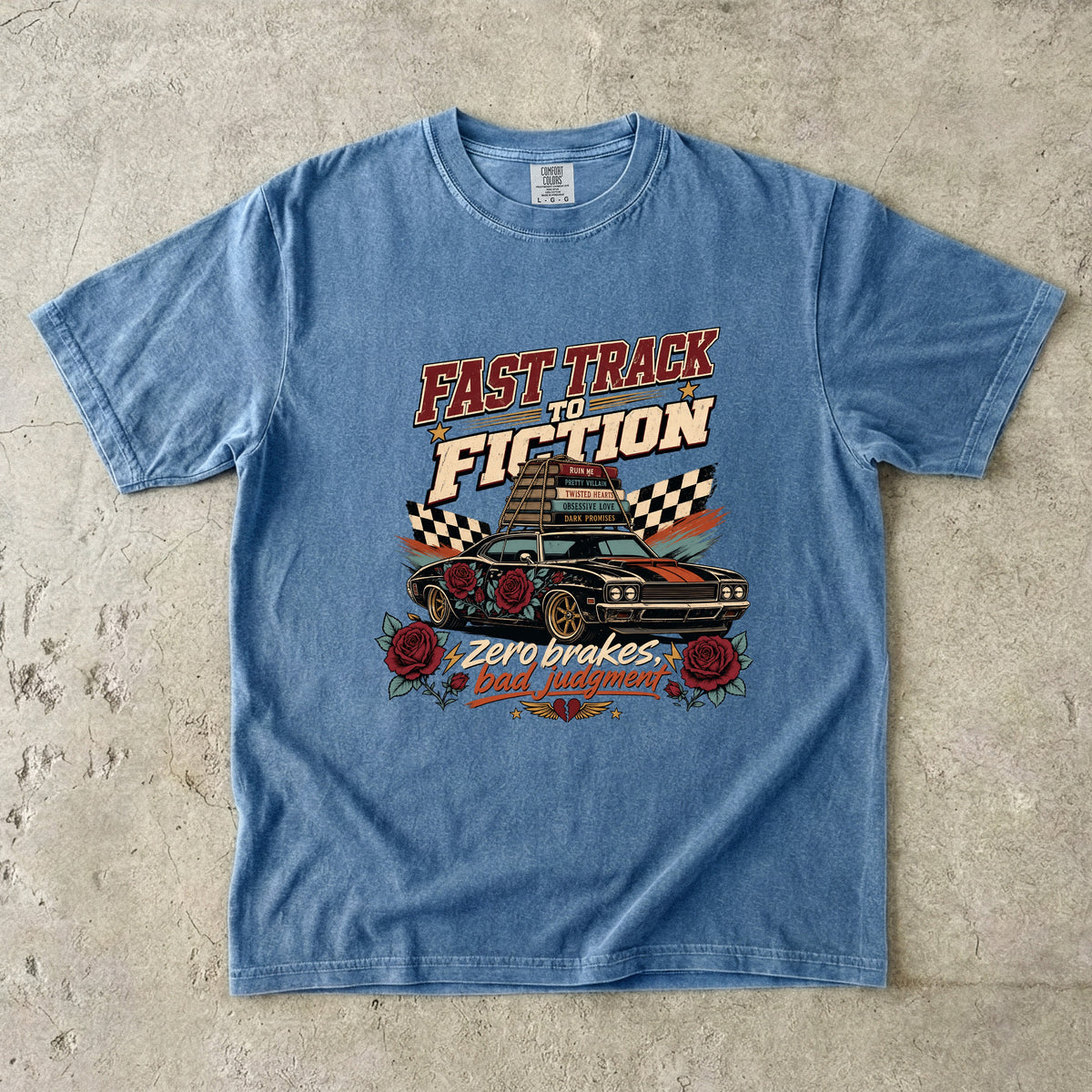 A light blue short-sleeve graphic t-shirt laid flat on a textured concrete surface. The graphic features a vintage-style car with roses and the text 'FAST TRACK TO FICTION' and 'Zero brakes.