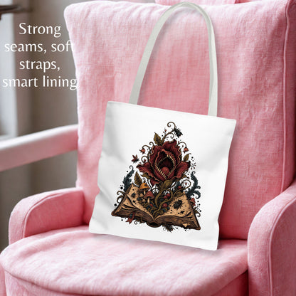 A white canvas tote bag with a gothic book illustration, resting on a pink armchair. The text on the left highlights its features: 'Strong seams, soft straps, smart lining'.