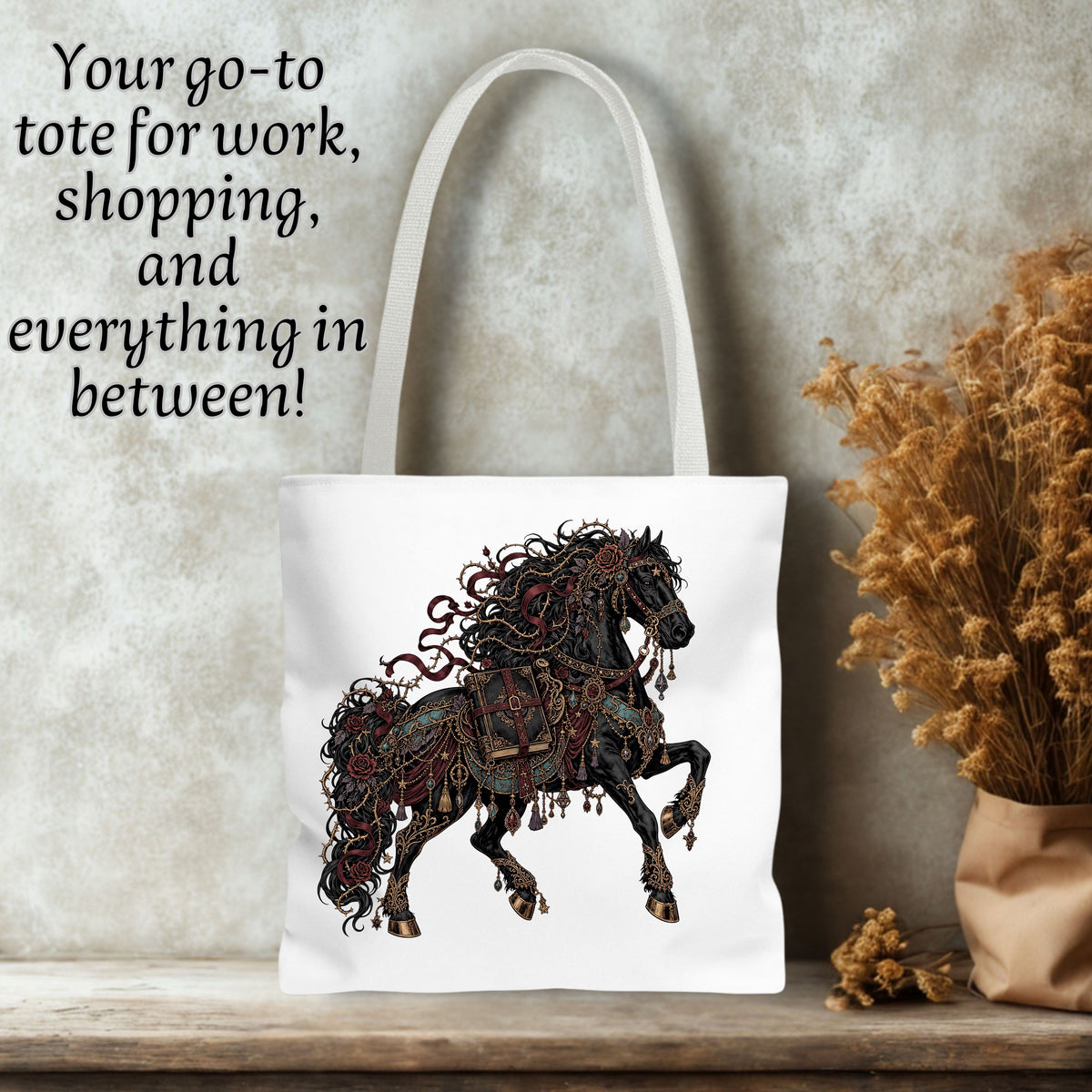 White canvas tote bag with a printed black and red decorative horse design, shown standing on a wooden surface against a textured wall with dried flowers and text on the left.