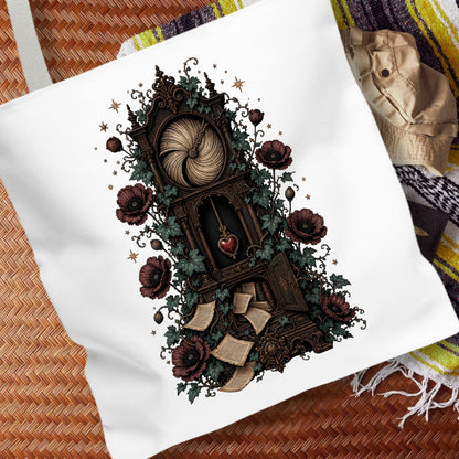 A white canvas tote bag featuring a detailed gothic illustration of a book with a heart-shaped page, surrounded by dark red roses, green ivy, and a large ball of yarn. The bag is displayed on a brown woven mat with a patterned blanket in the background.