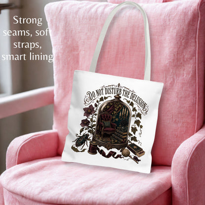 A white canvas tote bag with a vintage-style illustration of a bookshelf under a cage and the text 'DO NOT DISTURB THE DELIGHTS,' resting on a pink armchair. Text on the left highlights strong seams, soft straps, and smart lining.