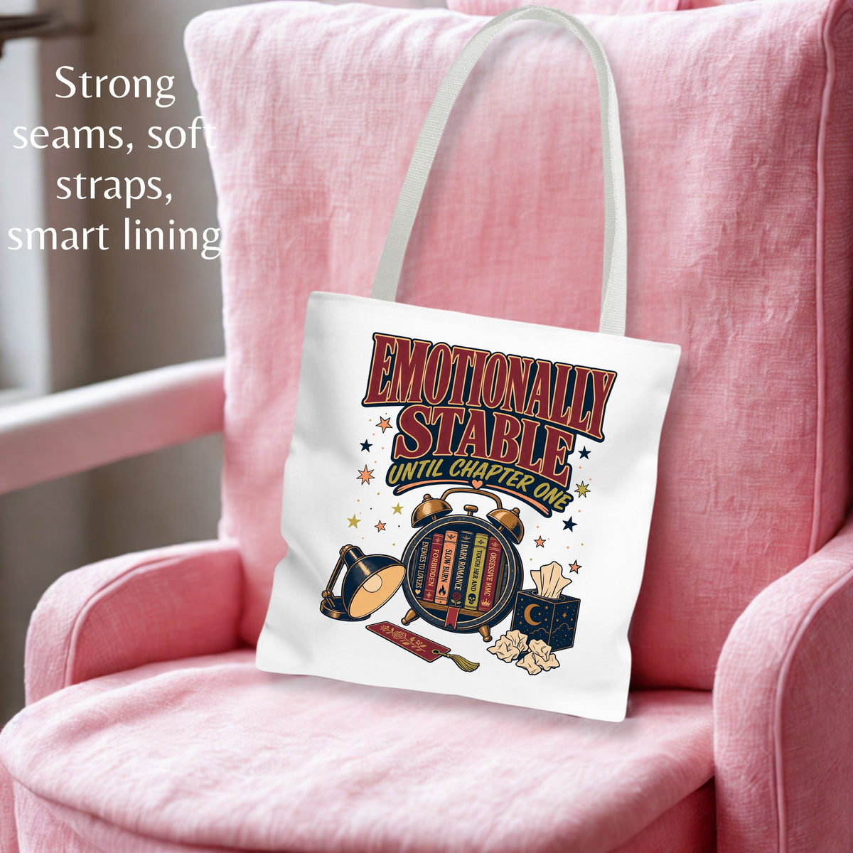 A white canvas tote bag with a colorful retro graphic reading 'Emotionally Stable Until Chapter 21' and illustrated alarm clocks, stars, and a tissue box, shown hanging on a pink armchair. Text on the left highlights strong seams, soft straps, smart lining, and a soft pink background.