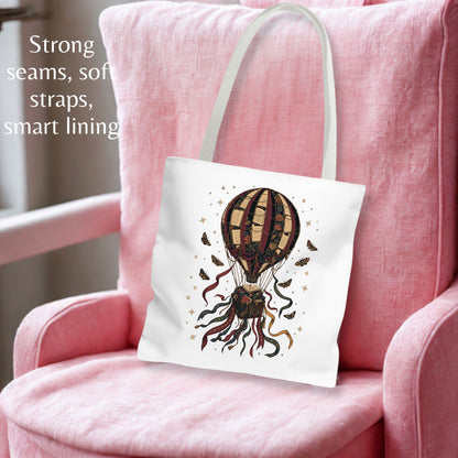 A white canvas tote bag with a whimsical hot air balloon illustration, resting on a pink armchair. The text on the left highlights its strong seams, soft straps, and smart lining.