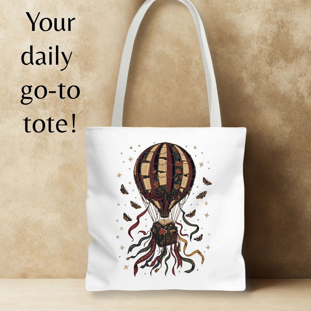 A white canvas tote bag with a vintage-style hot air balloon illustration in dark red, brown, and gold tones, displayed against a textured beige background with the text 'Your daily go-to tote!' on the left.