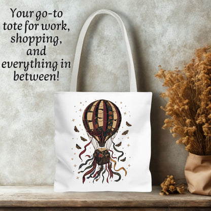 A white canvas tote bag with a printed hot air balloon illustration in earthy tones, displayed on a wooden surface against a textured gray wall with dried flowers and text overlay.