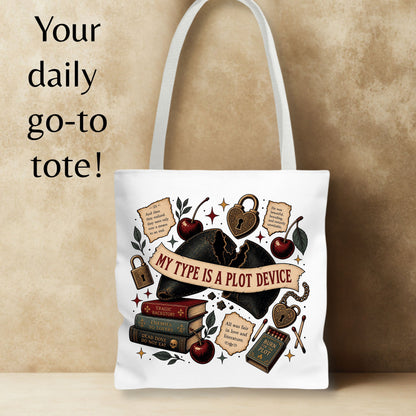 A white canvas tote bag with a gothic-themed graphic print featuring a black hat, books, cherries, padlocks, and the text 'MY TYPE IS A PLOT DEVICE'. The bag is displayed against a textured beige background with the text 'Your daily go-to tote!' on the left.