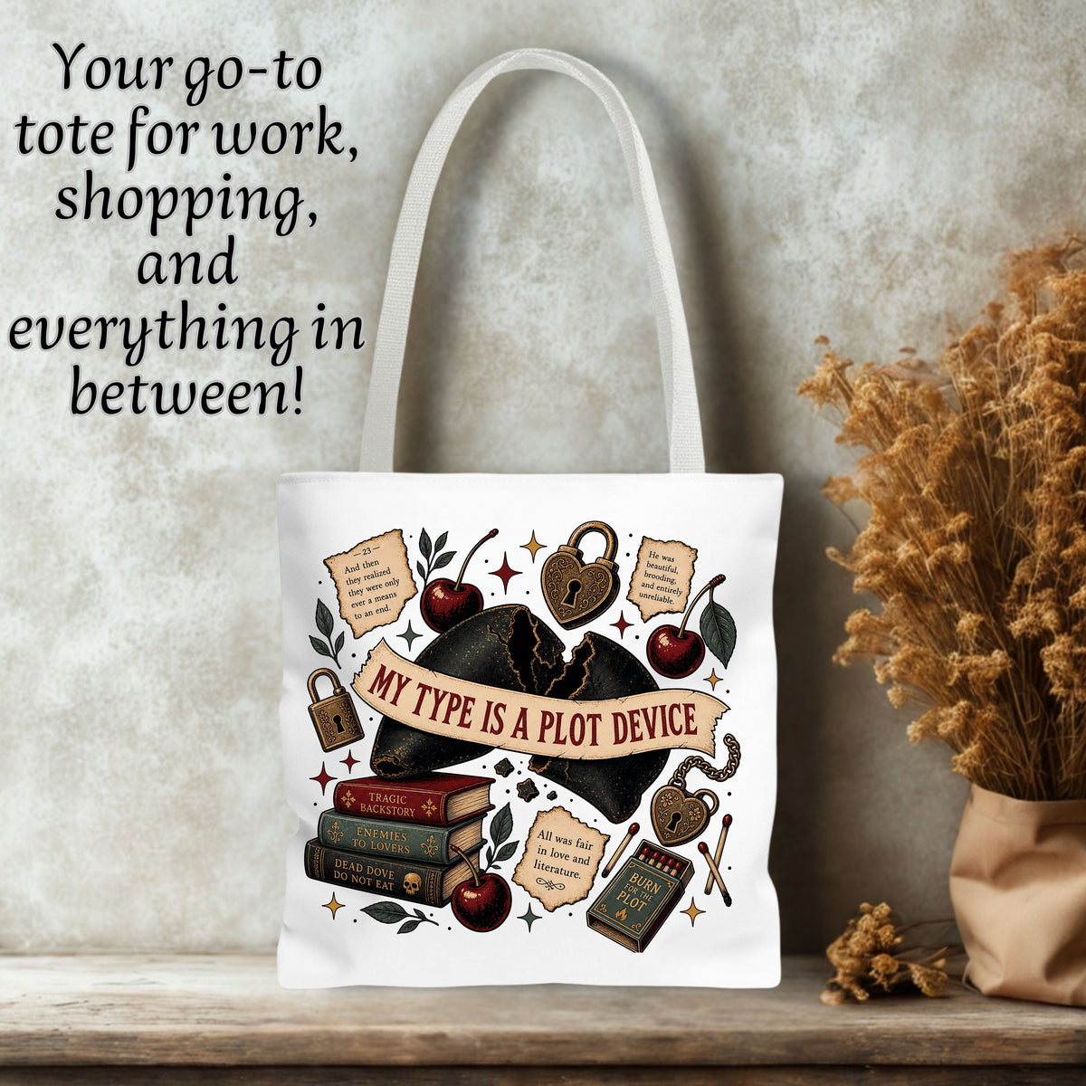 A white canvas tote bag with a vintage-style bookish illustration and the phrase 'MY TYPE IS A PLOT DEVICE' on the front, displayed on a wooden surface against a textured wall with dried flowers and text overlay.