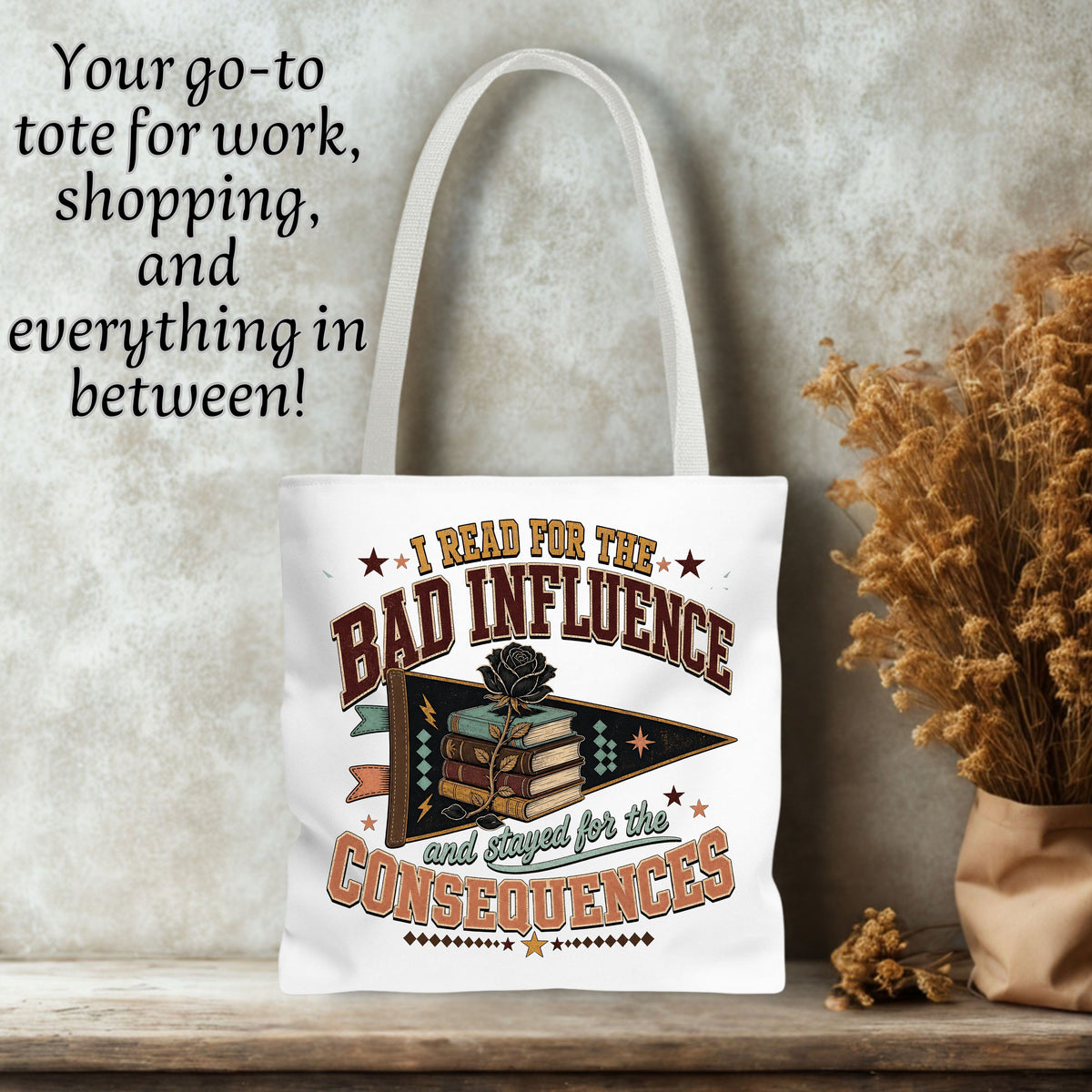 A white canvas tote bag with a vintage-style bookish graphic and text reading 'I READ FOR THE BAD INFLUENCE and Stayed for the CONSEQUENCES,' shown standing on a wooden surface against a textured wall with dried flowers and decorative text in the upper left.