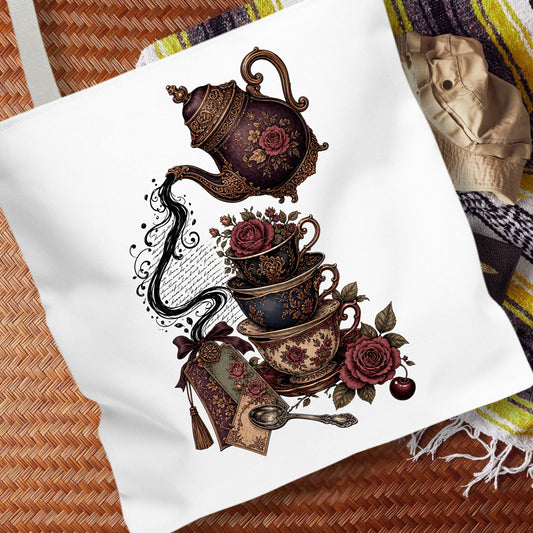 A white canvas tote bag featuring a vintage-style tea set graphic with a teapot, teacups, roses, and a teapot tag, displayed on a woven mat with a patterned blanket in the background.