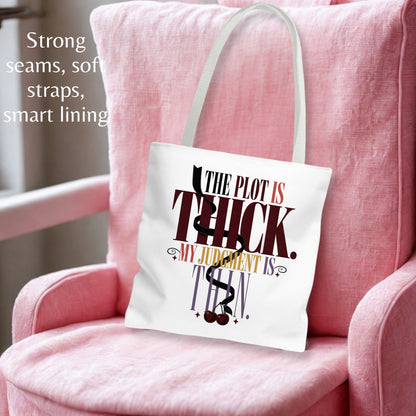 A white canvas tote bag with a black, red, and gold graphic text reading 'THE PLOT IS THICK. MY JUDGMENT IS THIN.