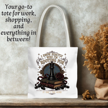 A white canvas tote bag with long handles, featuring a gothic chess-themed graphic print. The bag is displayed on a rustic wooden shelf against a textured gray wall, with dried flowers on the right and black text on the top left reading 'Your go-to tote for work, shopping, and everything in between!'.