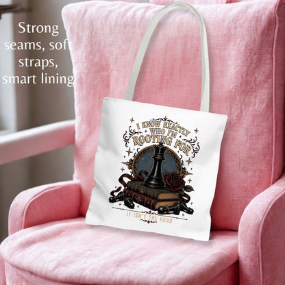 A white canvas tote bag with a graphic design of a chess piece, books, and roses, resting on a pink armchair. The text on the left highlights the bag's soft seams, straps, and smart lining.