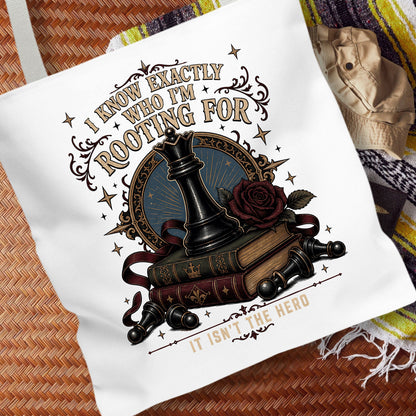 A white canvas tote bag with a detailed graphic print featuring a chess piece, books, a rose, and the text 'I KNOW EXACTLY WHO I'M ROOTING FOR IT ISN'T THE HERO'. The bag is displayed on a woven brown mat with a striped blanket in the background.