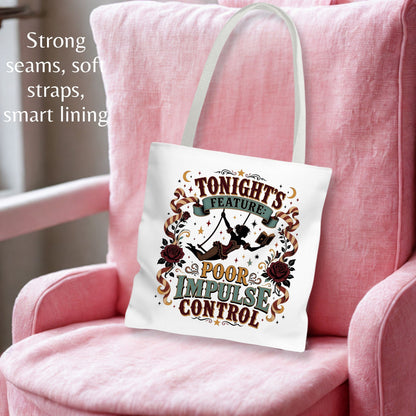 A white canvas tote bag with a vintage-style graphic reading 'TONIGHT'S FEATURE POOR IMPULSE CONTROL' sits on a pink upholstered chair. The bag has white shoulder straps and a printed design with dark red roses, gold swirls, and a black silhouette.