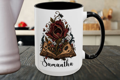 A white ceramic mug with a black handle and black interior, featuring a graphic of an open book with a large red flower and the name 'Samantha' printed below, shown on a dark wooden table in a kitchen setting.
