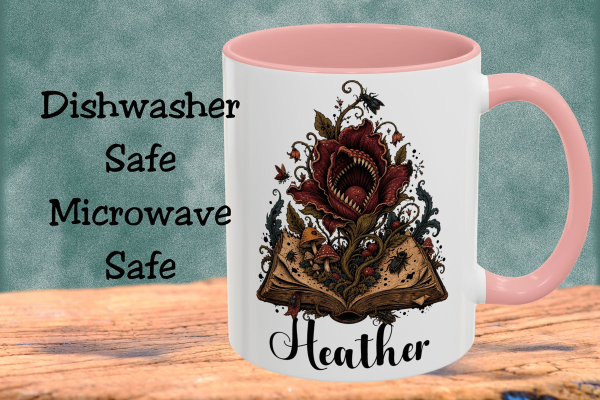 A white ceramic mug with a pink handle and interior, featuring a gothic illustration of an open book with a red rose and the name 'Heather' in black script. The mug is displayed on a wooden surface against a textured teal background with text reading 'Dishwasher Safe Microwave Safe'.