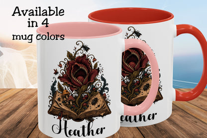 Two ceramic mugs shown on a wooden surface with a blurred beach background. The mugs are white with pink interiors and handles, featuring a dark red open book illustration with a spider and the name 'Heather' in black script.