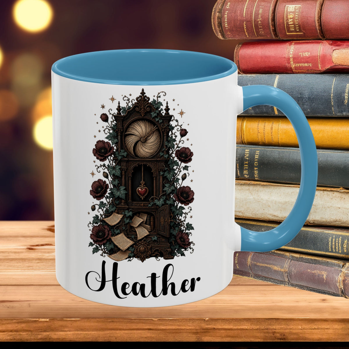A white ceramic mug with a blue interior and handle, featuring a gothic-style illustration of a clockwork mechanism with roses and the name 'Heather' printed below. The mug is styled on a wooden surface next to a stack of vintage books with a warm, blurred background.
