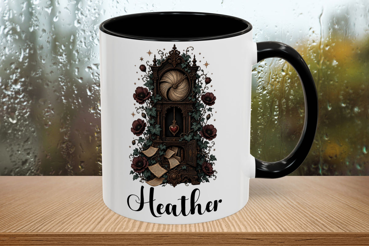 A white ceramic mug with a black handle and black interior, featuring a gothic-style illustration of a clock tower surrounded by dark roses and the name 'Heather' in script, set on a wooden surface with a blurred rainy window background.