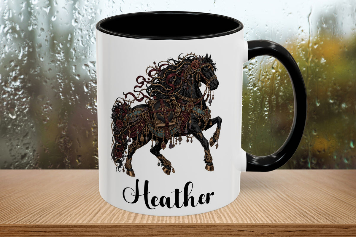 A white ceramic mug with a black handle and black interior, featuring a detailed black and brown illustration of a rearing horse and the name 'Heather' in black script near the bottom. The mug is shown on a wooden surface with a blurred rainy window background.