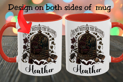 Two white ceramic mugs with red interiors and handles are shown side by side on a dark wooden surface with colorful blurred lights in the background. Black text at the top reads 'Design on both sides of mug,' and each mug features a gothic illustration of an ornate chair inside an arched frame with the text 'Do not disturb the delusion' and the name 'Heather' below.