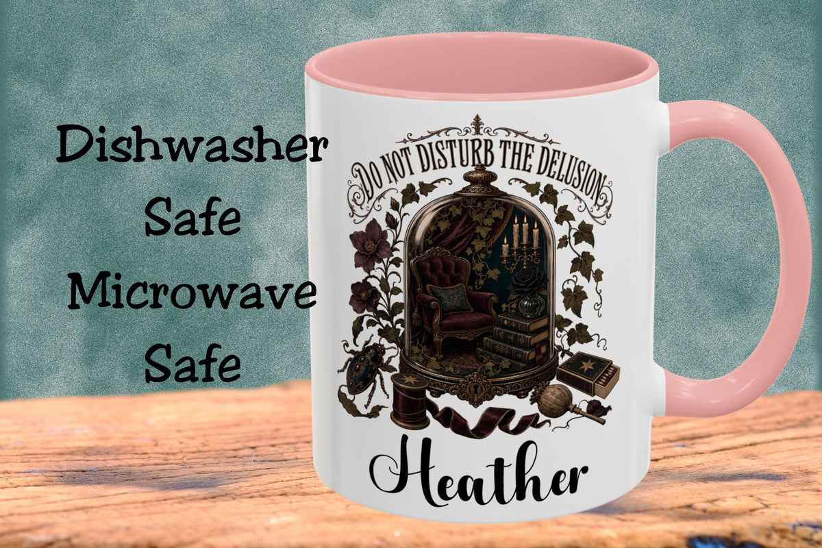 A white ceramic mug with a pink interior and handle, featuring a gothic-style illustration and the text 'DO NOT DISTURB THE DELUSION Heather' on the front. The mug is shown on a wooden surface against a textured teal background, with the words 'Dishwasher Safe Microwave Safe' printed on the left.