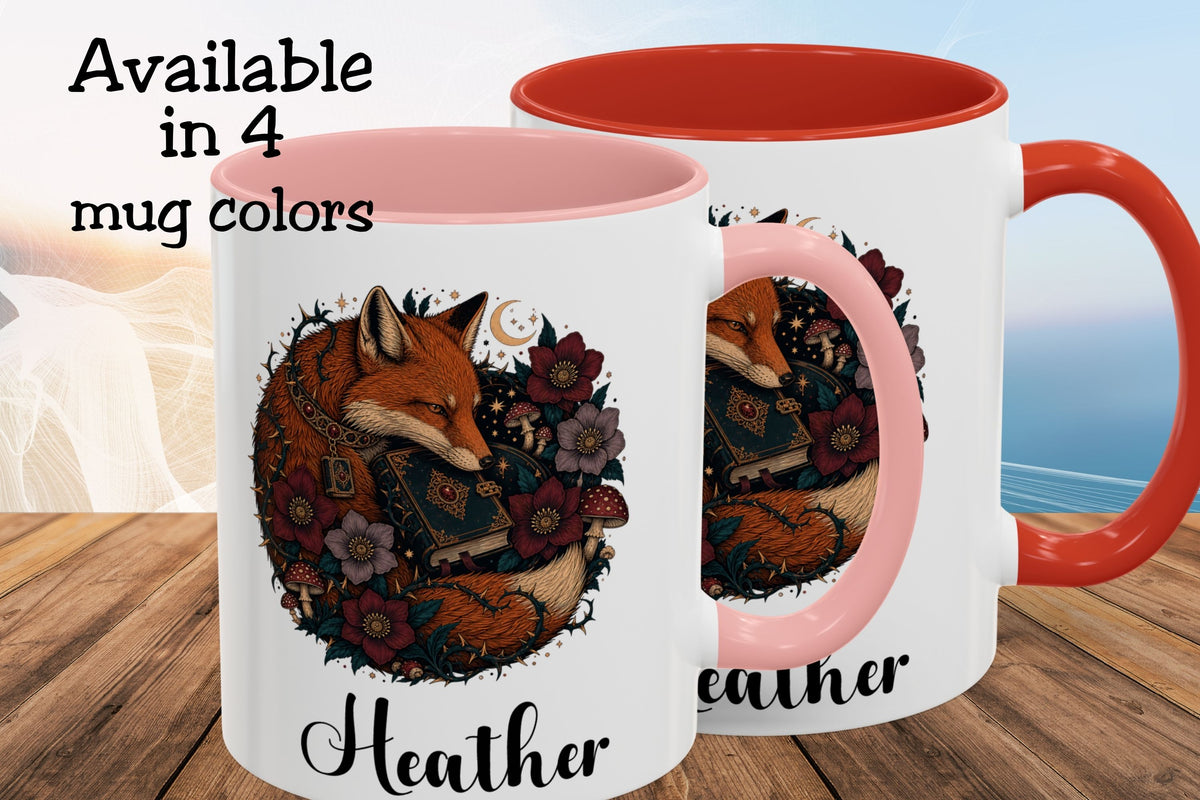Two ceramic mugs shown on a wooden surface with a blurred beach background. The mugs are white with pink interiors and handles, featuring a printed illustration of a fox surrounded by flowers and books, with the name 'Heather' in script at the bottom.