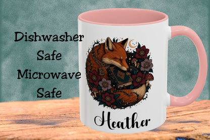 A white ceramic mug with a pink interior and handle, featuring a printed illustration of a fox surrounded by flowers and the name 'Heather' in script. The mug is shown on a wooden surface against a textured teal background, with text on the left reading 'Dishwasher Safe Microwave Safe'.
