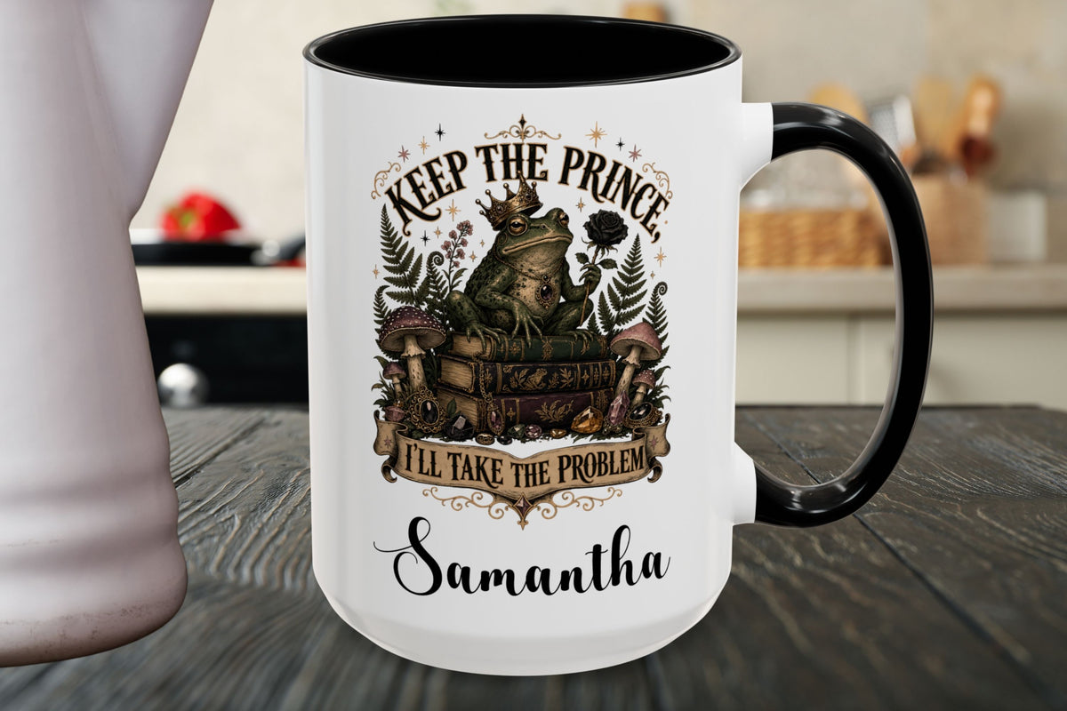 A white ceramic mug with a black handle and black interior, featuring a vintage-style graphic of a prince and fairy with the text 'KEEP THE PRINCE, I'LL TAKE THE PROBLEM' and the name 'Samantha' printed below, set on a dark wooden table.