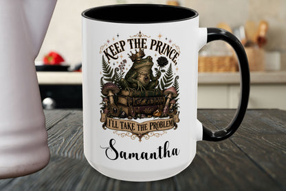 A white ceramic mug with a black handle and black interior, featuring a vintage-style graphic of a prince and fairy with the text 'KEEP THE PRINCE, I'LL TAKE THE PROBLEM' and the name 'Samantha' printed below, set on a dark wooden table.