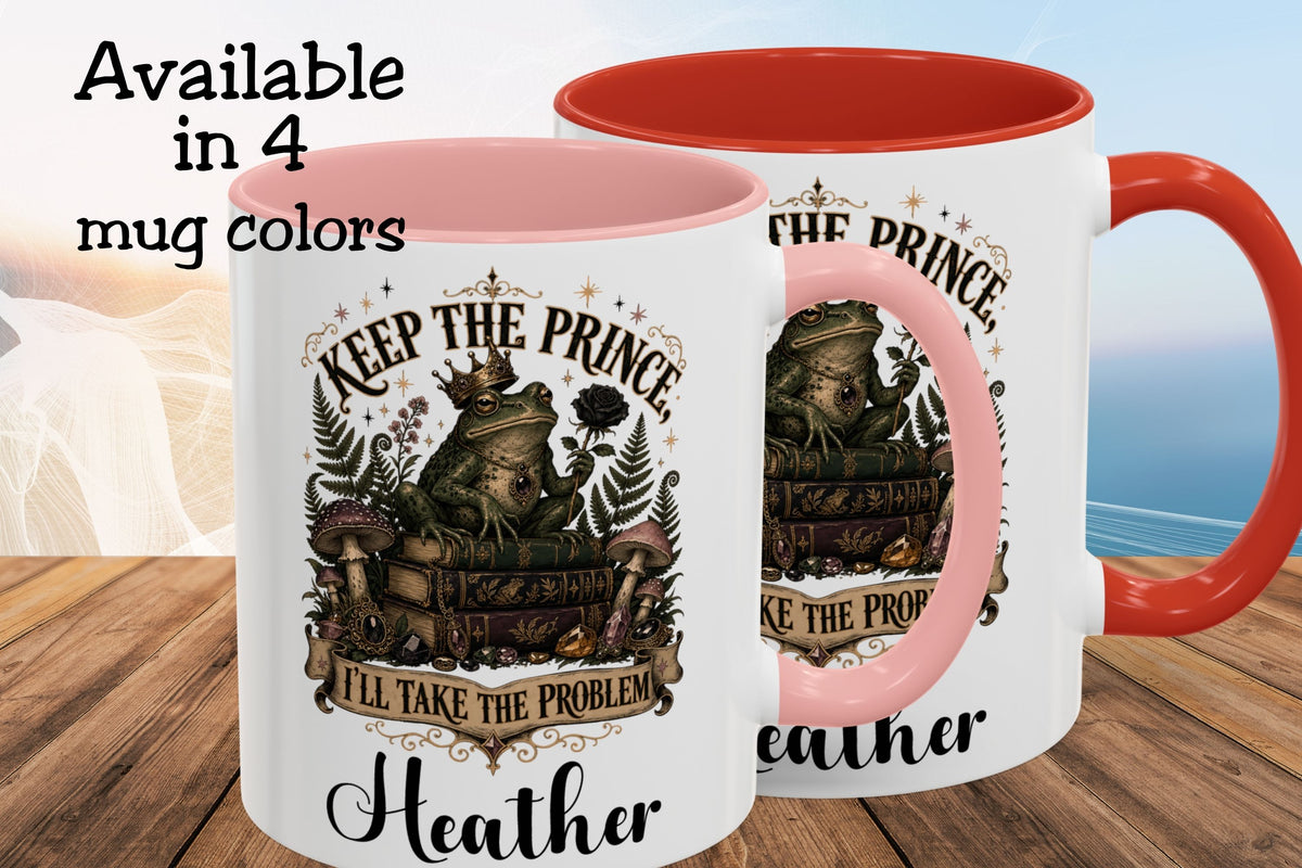 Two white ceramic mugs with red interiors and handles, shown on a wooden surface with a blurred beach background. The front mug has a printed graphic of a frog on a suitcase with the text 'KEEP THE PRINCE, I'LL TAKE THE PROBLEM' and the name 'Heather' below.
