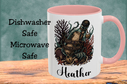 A white ceramic mug with a pink interior and handle, featuring a vintage-style ocean illustration with a bottle labeled 'Lost at Sea' and the name 'Heather' printed below. The mug is shown on a wooden surface against a textured teal background, with the words 'Dishwasher Safe Microwave Safe' displayed on the left.