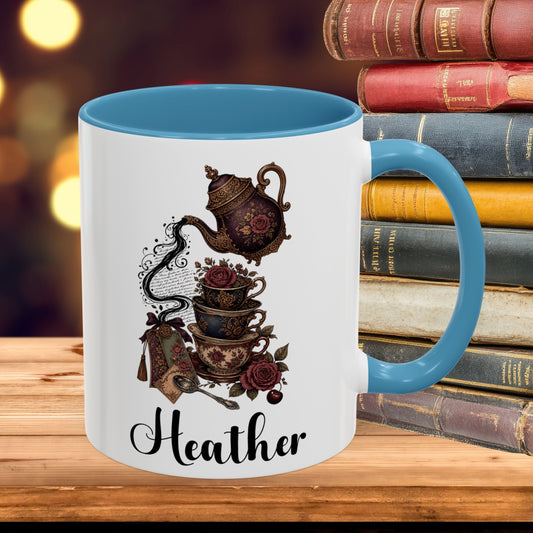 A white ceramic mug with a blue interior, handle, and rim, featuring a vintage tea set illustration and the name 'Heather' in black script. The mug is set on a wooden surface next to a stack of books with a blurred warm background.